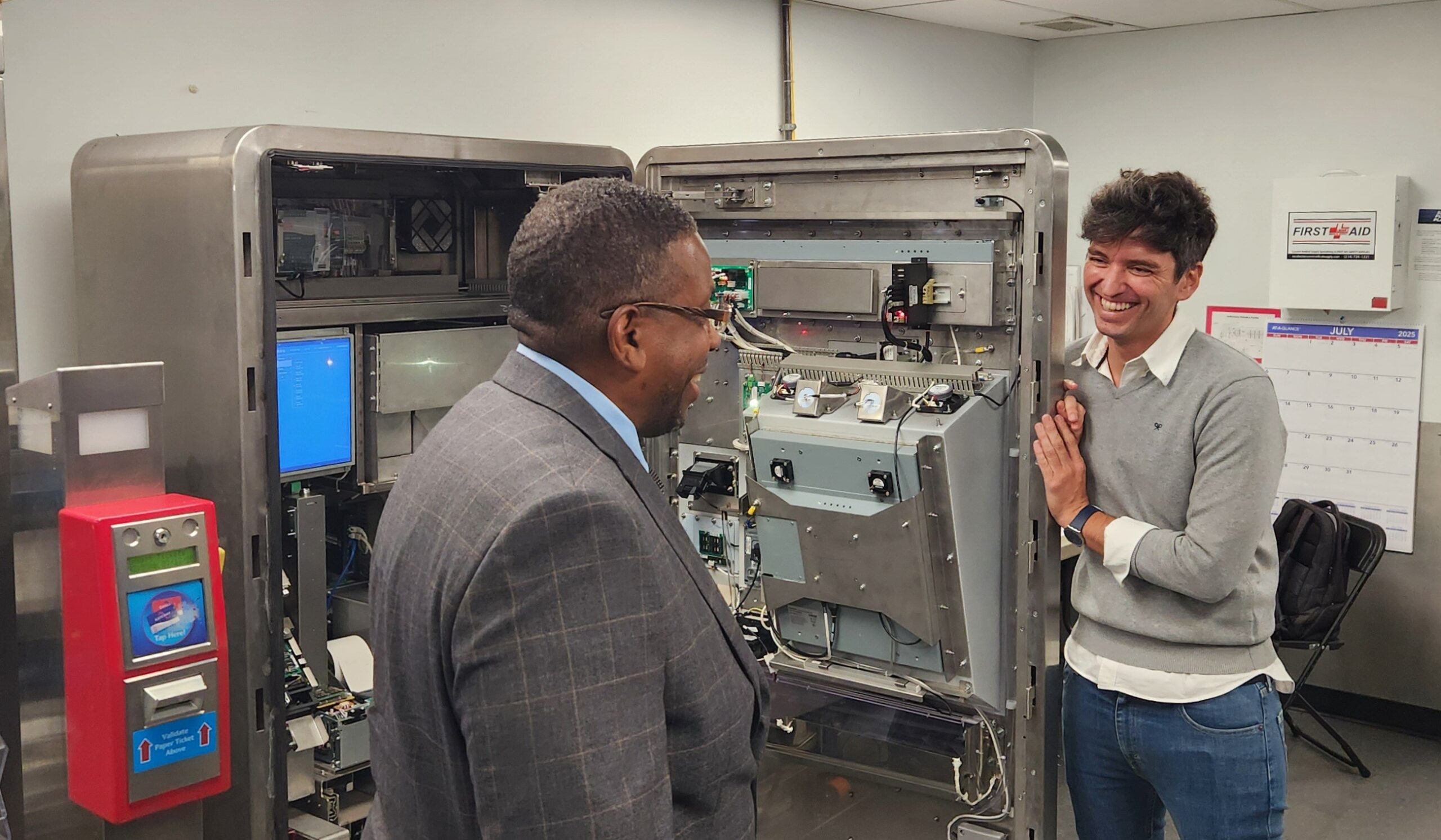 Two people stand near an opened ticket vending machine.