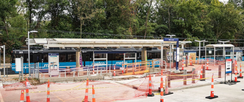 UMSL South Station with construction in the foreground and a train passing through the station in the background